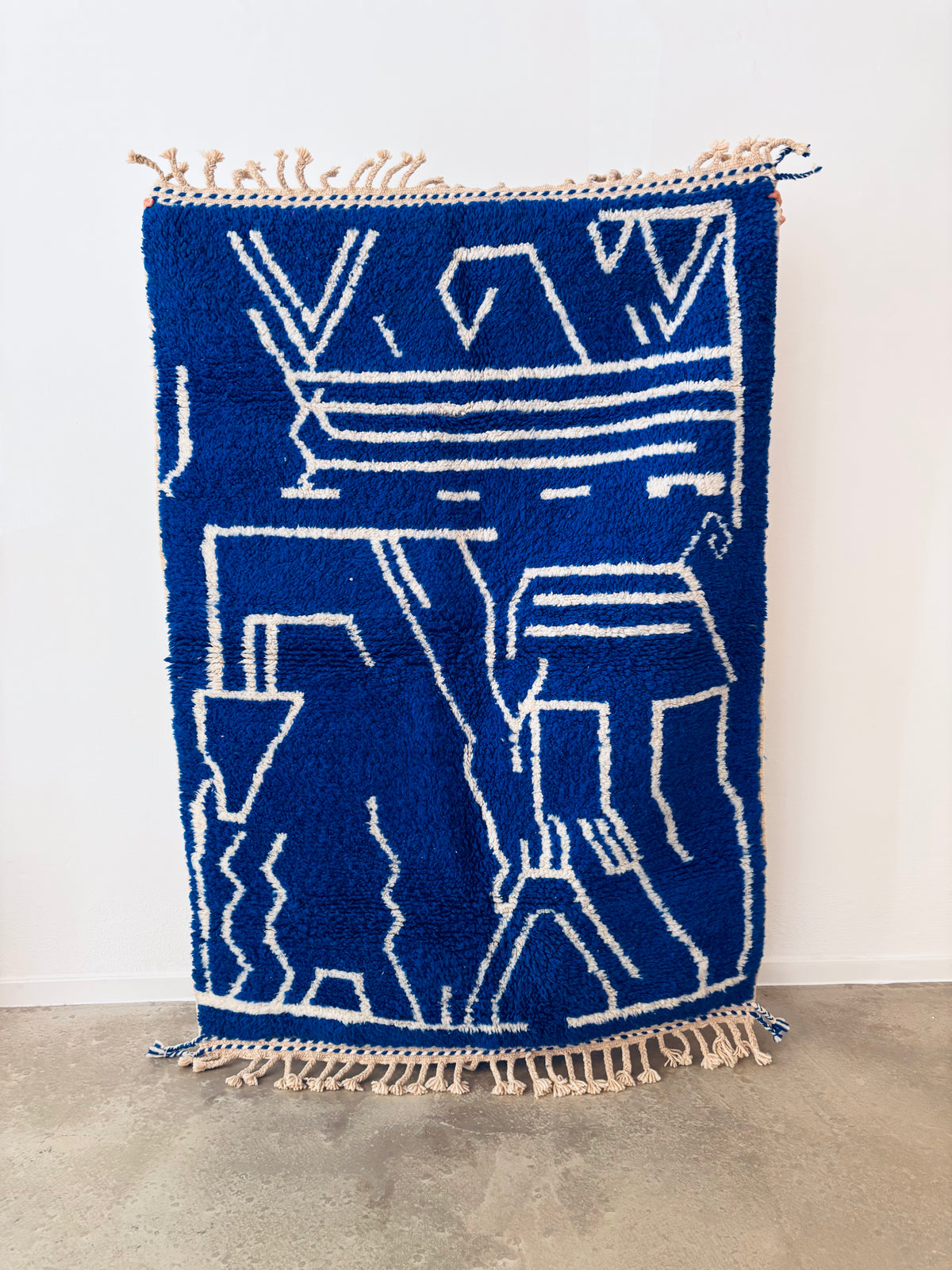 Handgeknüpfter Berberteppich im Beni-Ourain-Stil in Cremeweiß mit geometrischem Muster in Blau und Rosa, ausgelegt auf einem hellen Holzboden in einem modern eingerichteten Raum mit natürlichem Lichteinfall