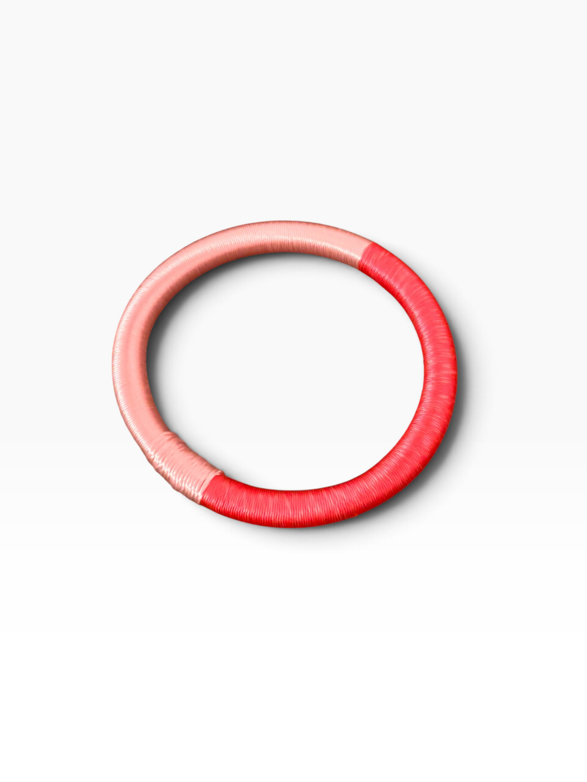 Der Armreif „Minama – Koralle-Pink“ von LEY! aus rosa und rotem Garn wird auf weißem Hintergrund präsentiert.