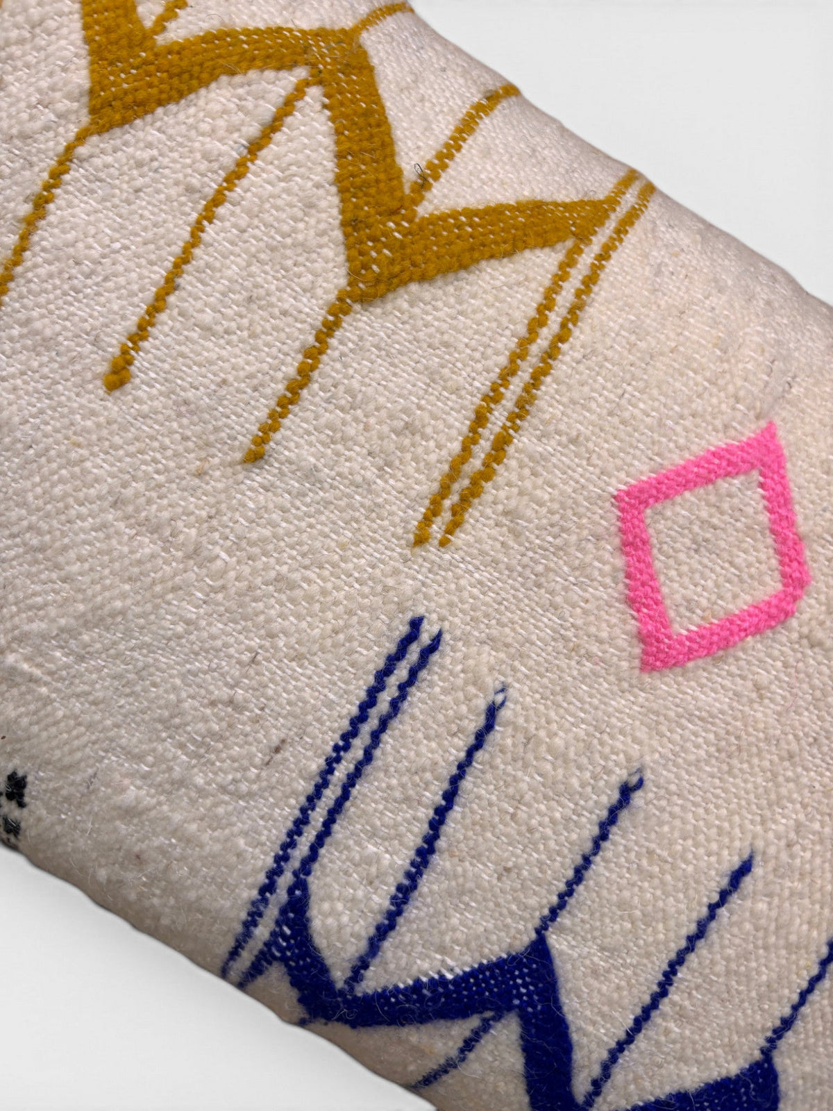 Eine Nahaufnahme des LEY! Kissen - Colorful Line 40x60 von LEY! mit gelben, blauen Zickzacklinien und einer rosa Raute.