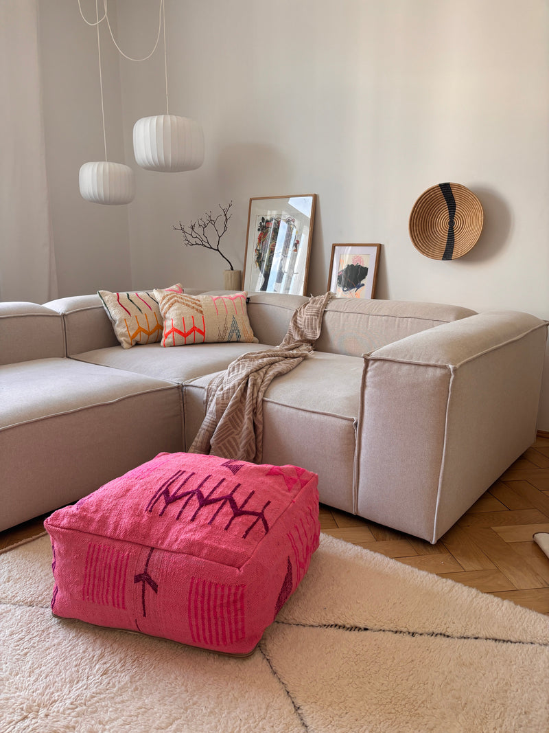 Ein modernes Wohnzimmer mit einer beigen Couchgarnitur, bunten Kissen, Kunst und einer LEY! Bodenkissen - Colorful Line - Pink Edition.