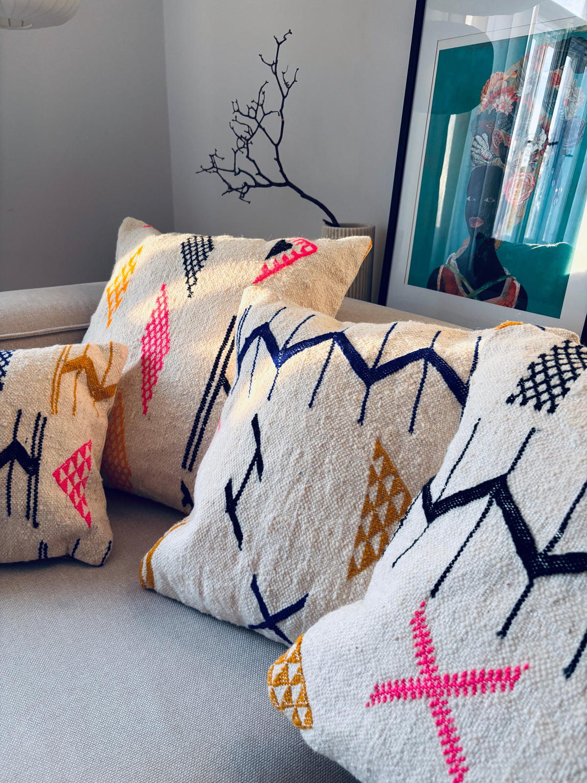 Vier LEY!-Kissen – Colorful Line – cremefarbene Kissen im Format 50 x 50 mit bunten geometrischen Stickereien auf einem Sofa.