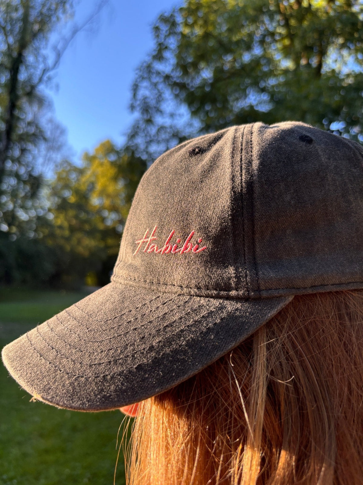 Eine Person trägt die LEY! „Habibi“-Kappe in Rosa mit verstellbarem Verschluss im Freien zwischen Bäumen und im Sonnenlicht.