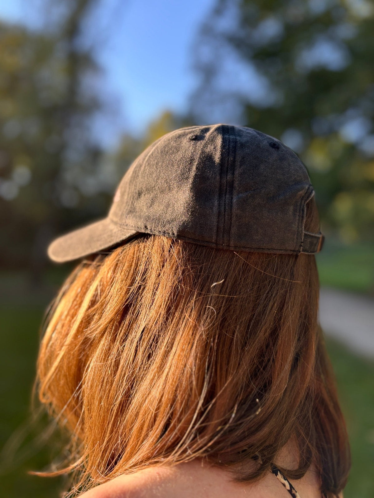 Eine Frau mit braunen Haaren trägt die LEY! „Habibi“-Kappe in Rosa und steht im Freien mit dem Rücken zur Kamera.