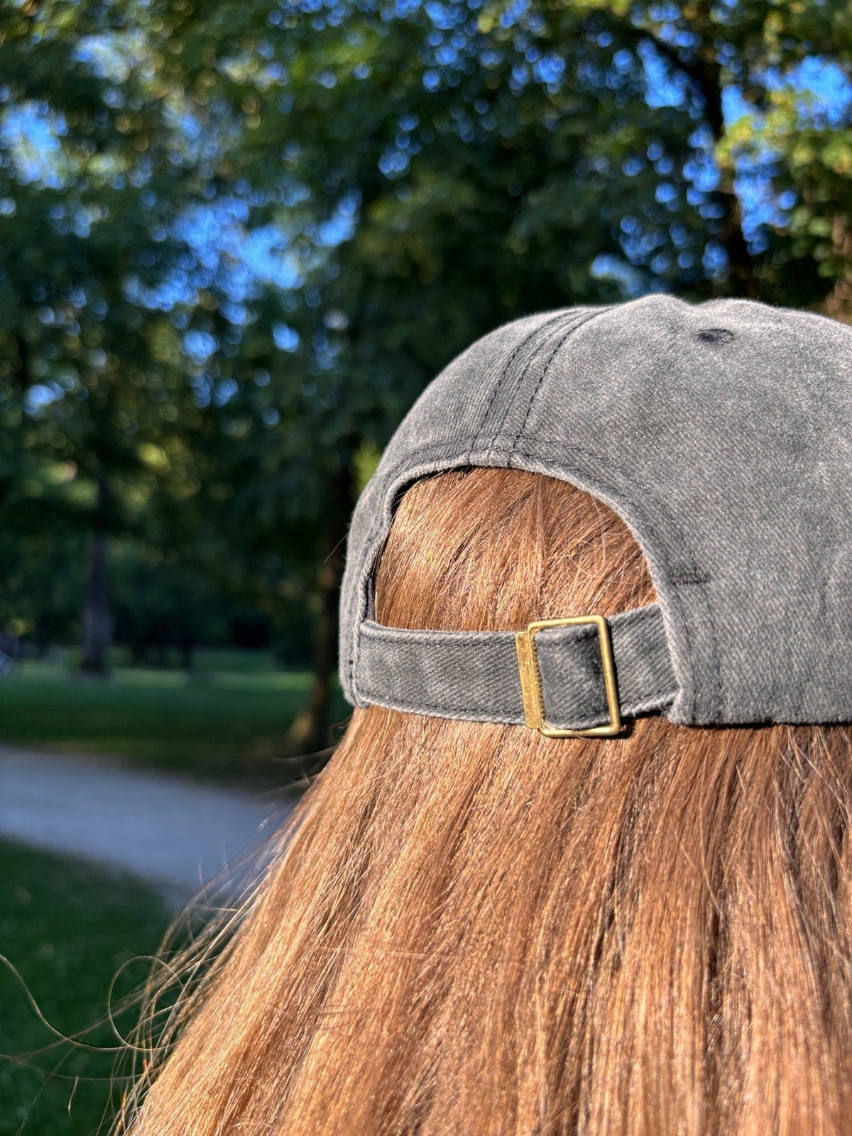 Eine Person mit langen braunen Haaren trägt die LEY! „Habibi“-Kappe in Rosa im Freien, im Hintergrund sind Bäume und Sonnenlicht zu sehen.