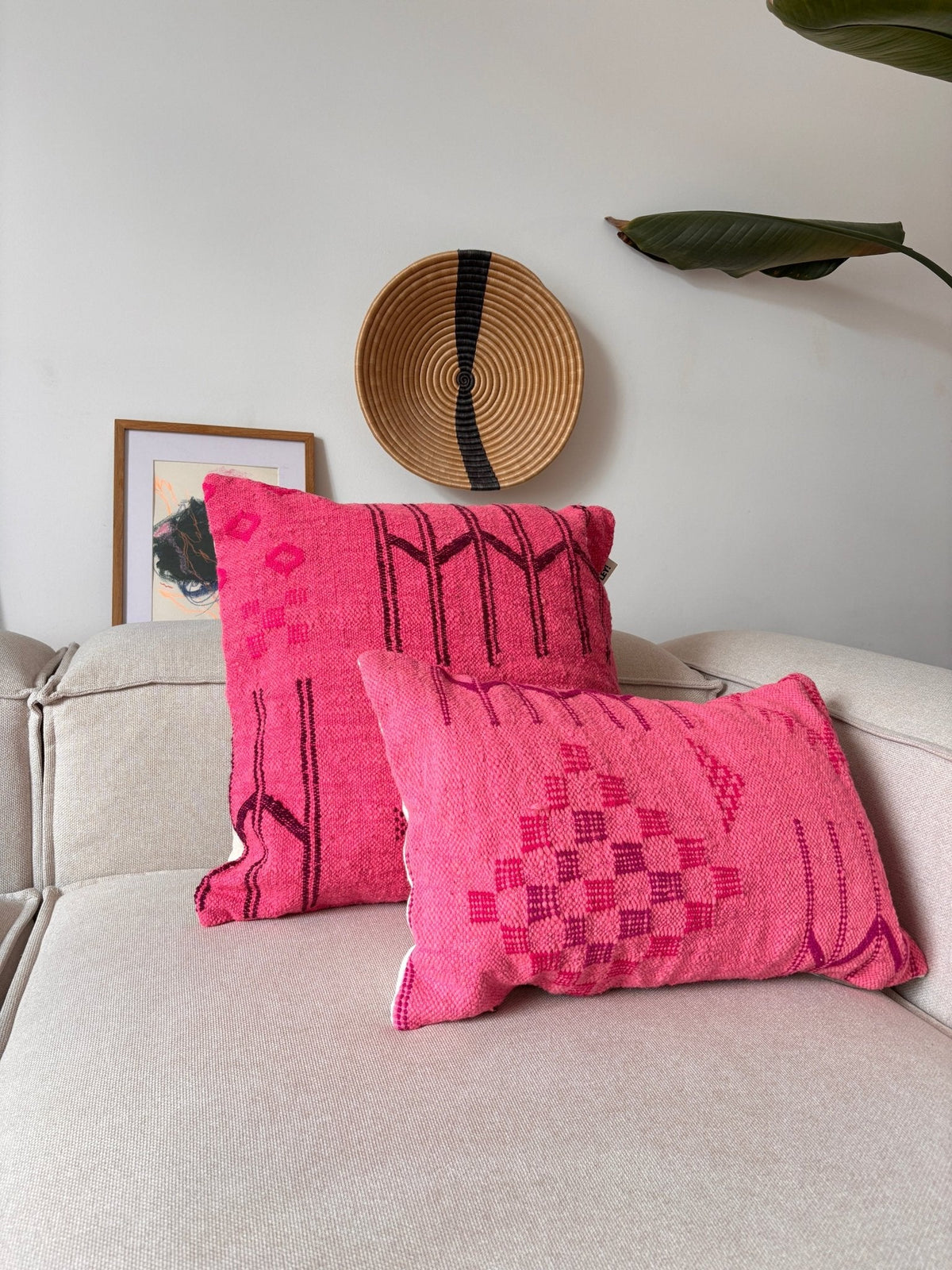 Zwei Kissen der Serie „LEY! Kissen – Colorful Line – Pink Edition“, 50 x 50 cm, auf einem beigen Sofa mit einem Korb und Wanddekoration.