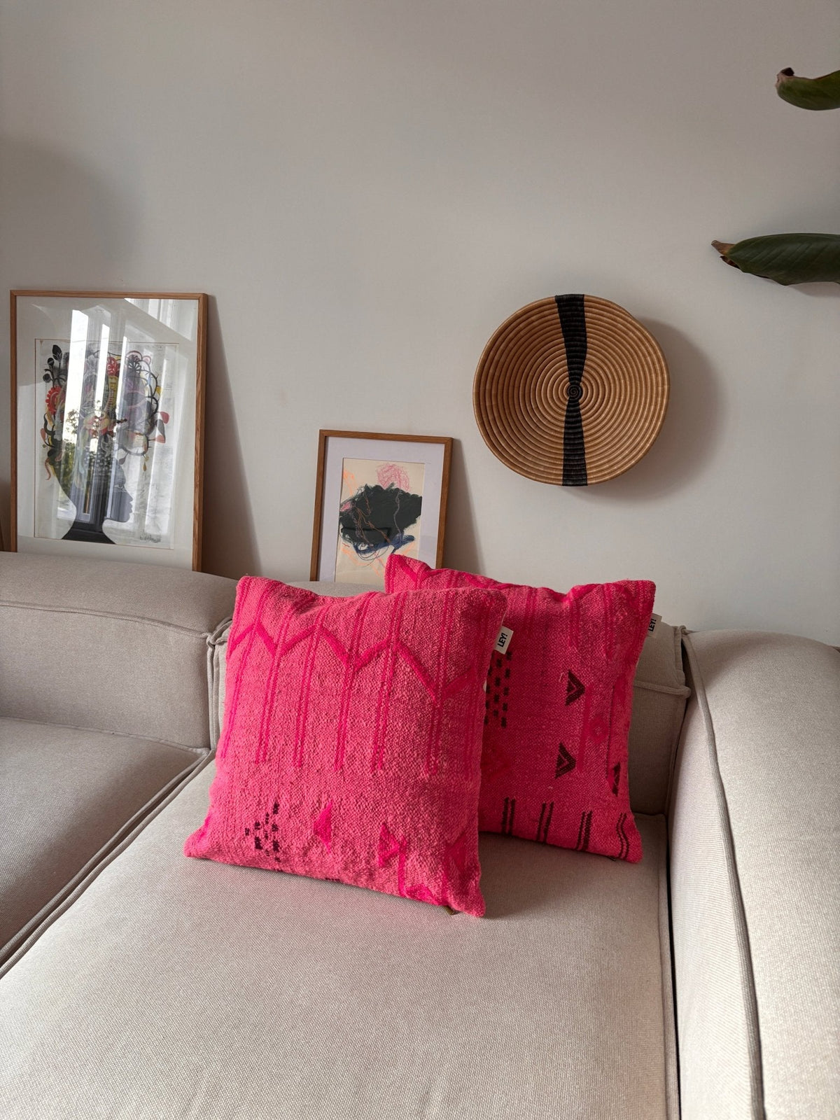 Zwei LEY!-Kissen – Colorful Line – Pink Edition, 50 x 50 cm, auf einem beigen Sofa, mit Wandbild und Korb vor einer hellen Wand.