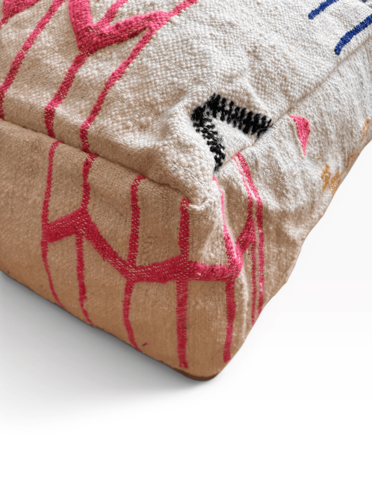 LEY! Bodenkissen – Colorful Line – Juni: Beiges Boho-Kissen mit pink-schwarzen Mustern auf weißem Hintergrund aus Wolle.