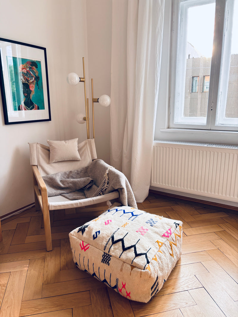 Gemütlicher Sessel, Wolle-Decke, LEY! Bodenkissen – Colorful Line – Lavina, moderne Lampe, gerahmte Bilder, transparente Vorhänge.