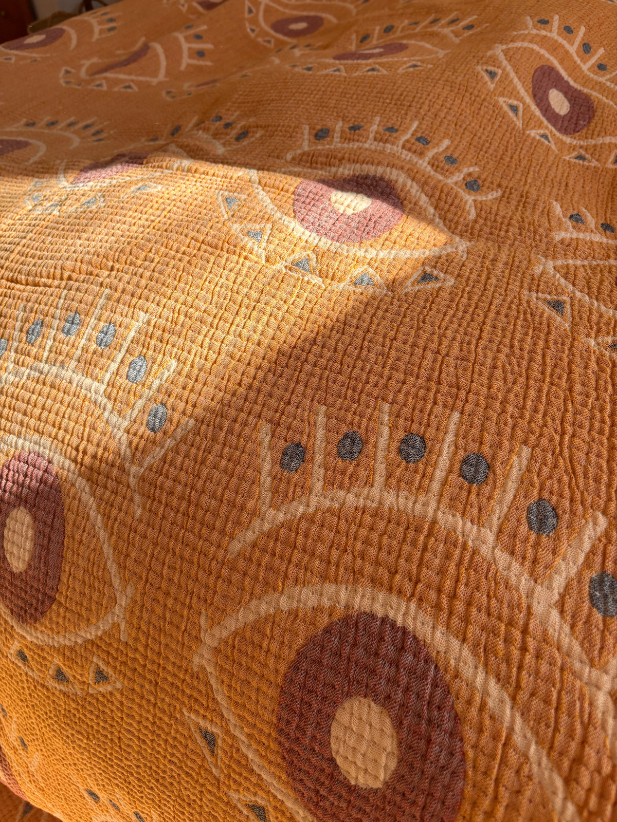 Eine Nahaufnahme der LEY! Musselin Decke - Vision in Gelb-Blau (2,20 x 2,50 m) zeigt im Sonnenlicht abstrakte Augenmuster in Beige, Braun und Grau - ideal, um Ihrem Raum ein Boho-Design-Flair zu verleihen.