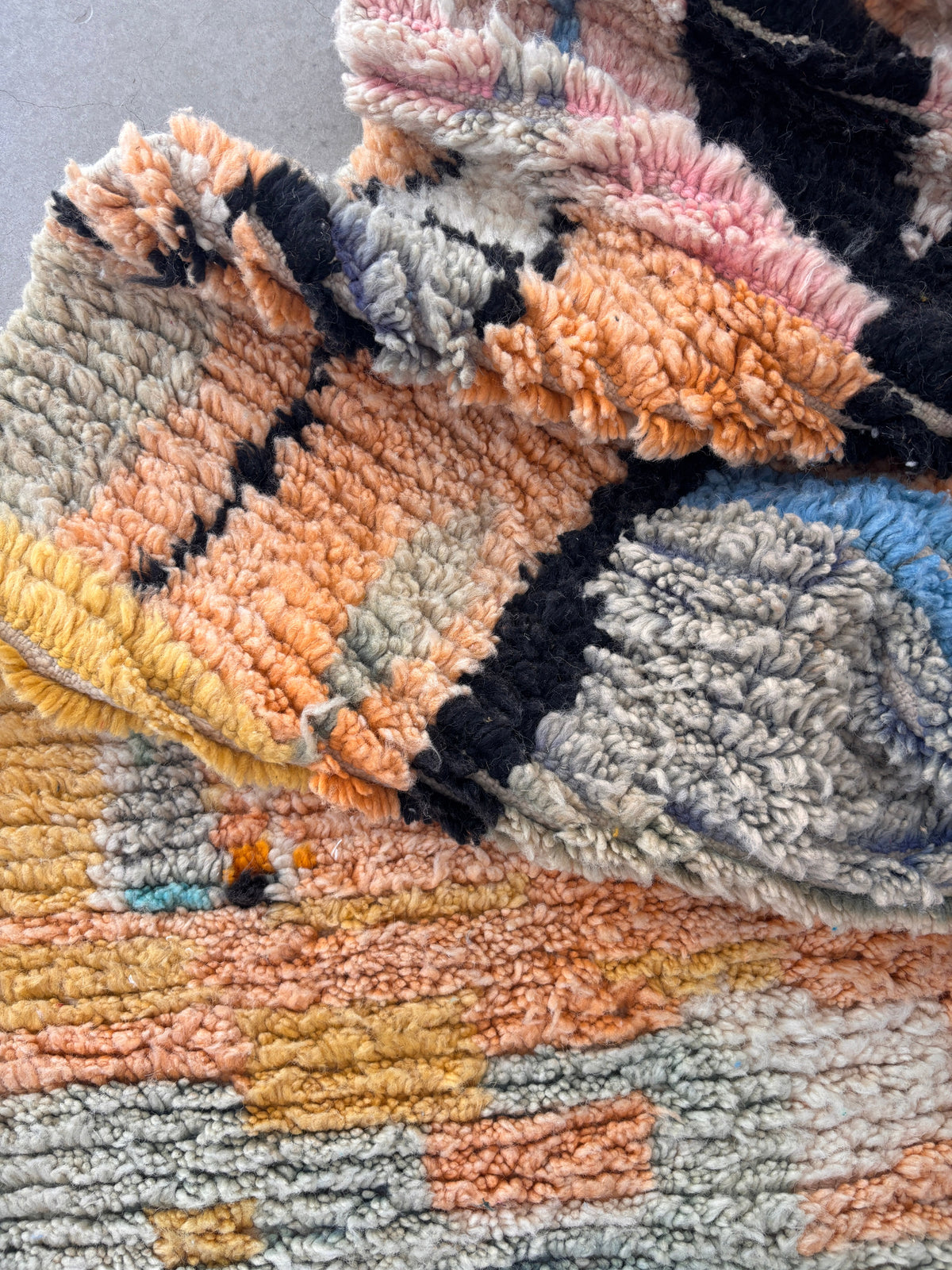 Eine Nahaufnahme des LEY! Berber Teppich - Biama (1,60 x 2,60), handgewebt aus Schurwolle, zeigt seinen dicken, weichen Flor, die detaillierten Nähte und die abstrakten Muster in Pfirsich, Grau, Gelb, Schwarz und Blau.