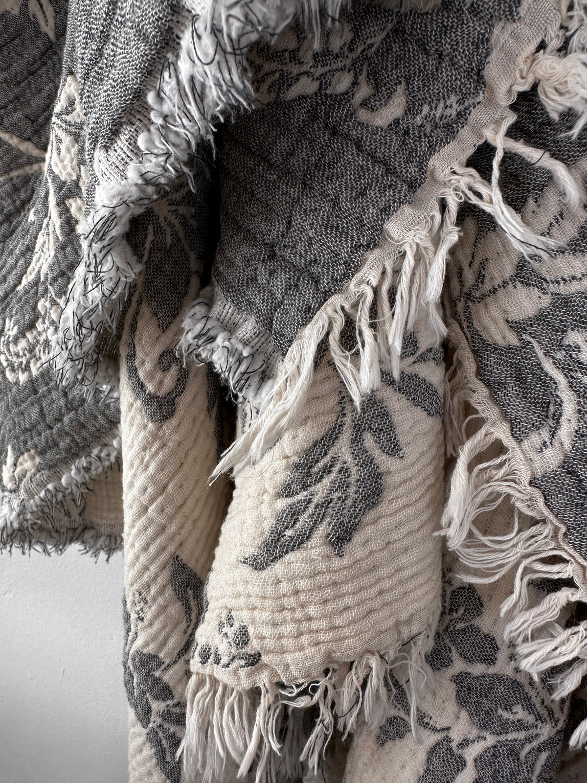 Nahaufnahme der LEY! Musselin Decke - ROSE in Grau-Weiß (2,20 x 2,50 m) mit floralem Muster, ausgefransten Kanten und Boho-Design. Das weiche, mehrlagige Material sorgt für einen gemütlichen, rustikalen Look.