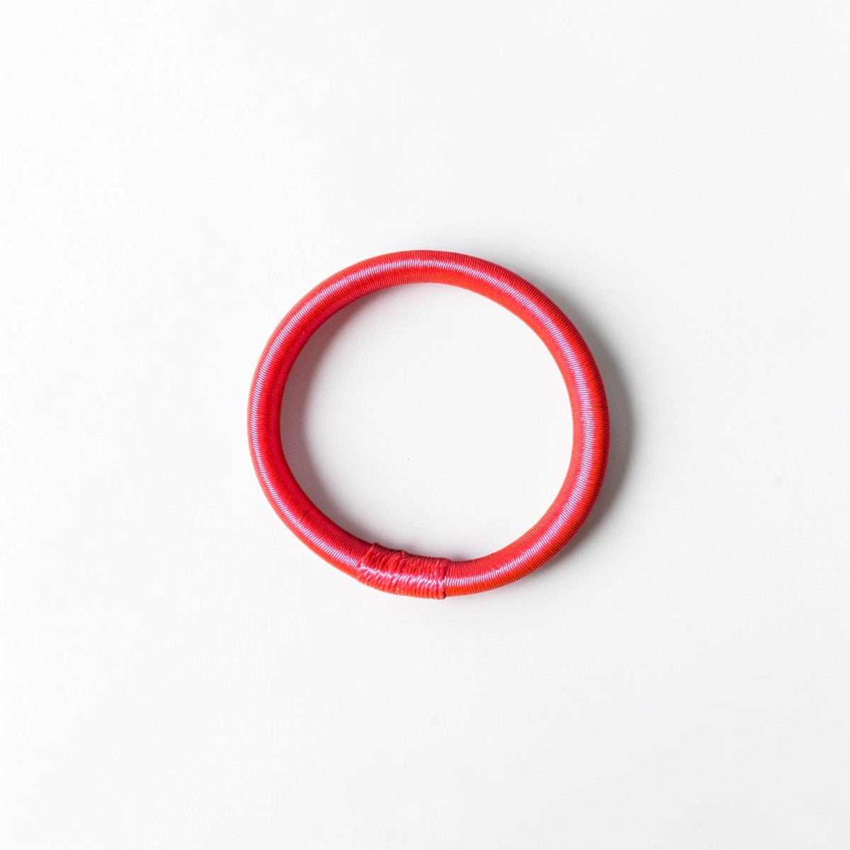 Ein neonpinker Armreif von LEY!, inspiriert von Garn Schmuck, liegt auf einem schlichten weißen Hintergrund.