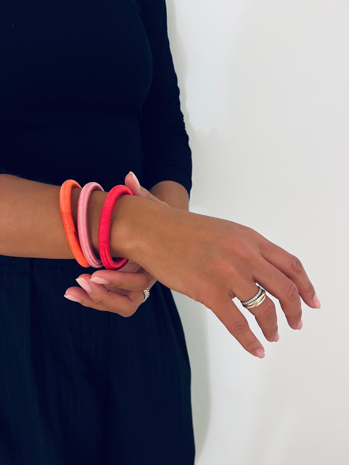 Eine Person in schwarzer Kleidung passt einen LEY! Minama-Armreif in Minzgrün und rosa Armreifen an und trägt dabei einen silbernen Ring vor einem schlichten Hintergrund.
