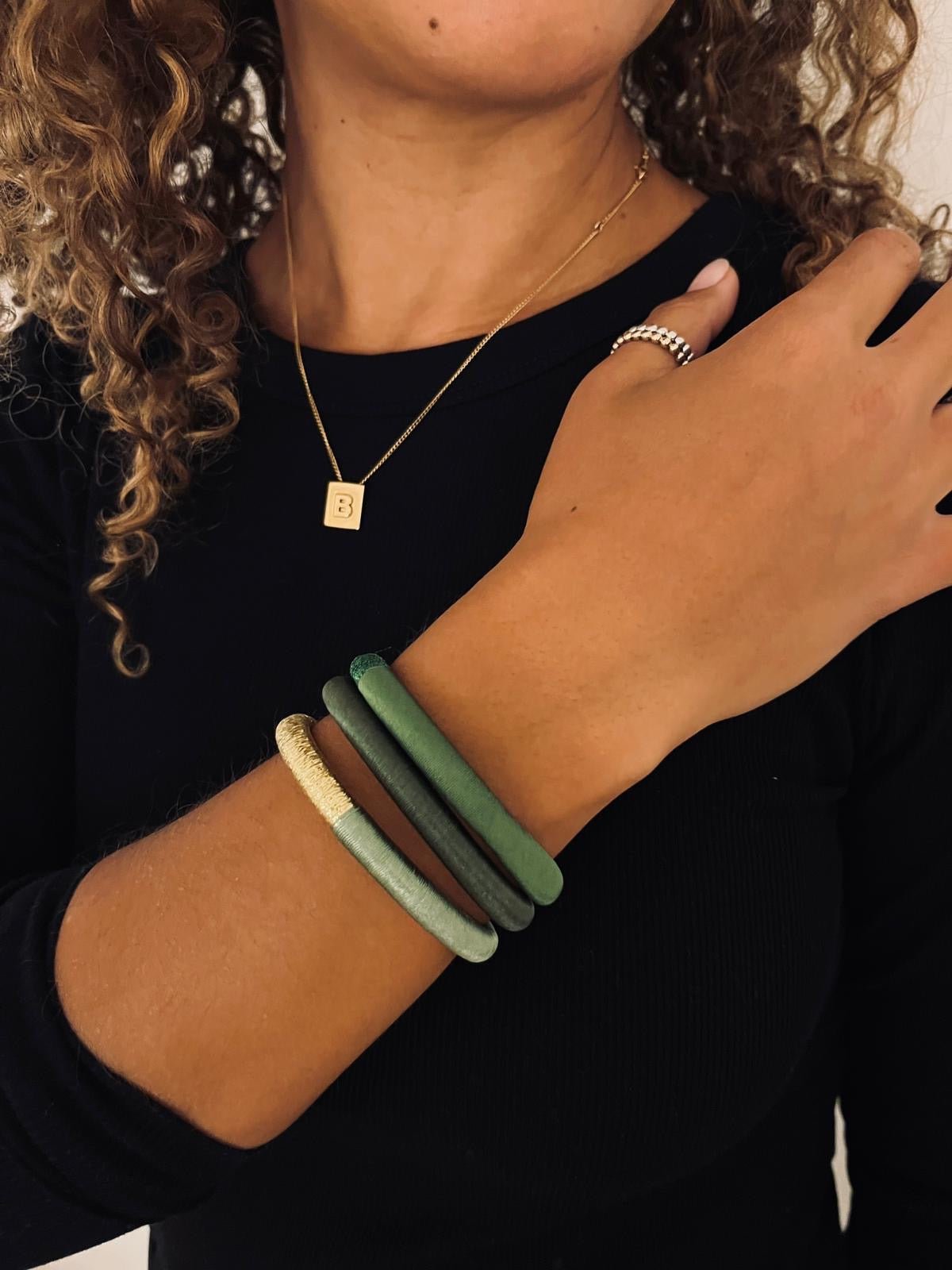 Eine Person mit lockigem Haar trägt eine goldene Halskette und den Armreif „LEY! – Minama – mint“ sowie ein schwarzes Oberteil.