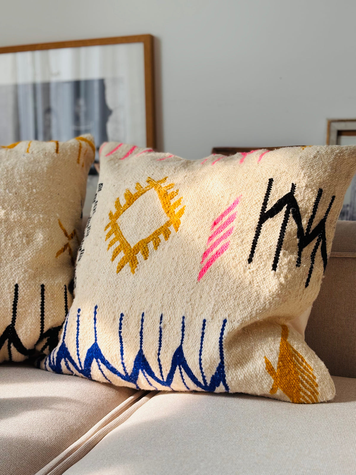 LEY! Kissen - Colorful Line, 60 x 60 von LEY!, mit geometrischen Mustern auf einer beigen Couch in einem sonnenbeschienenen Raum.