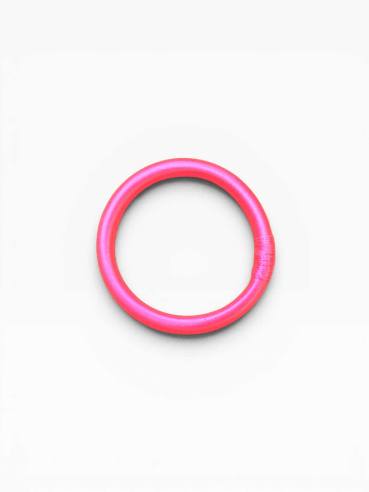 Ein neonpinker Armreif – „Minama“ von LEY! – ist in der Mitte eines schlichten weißen Hintergrunds abgebildet.
