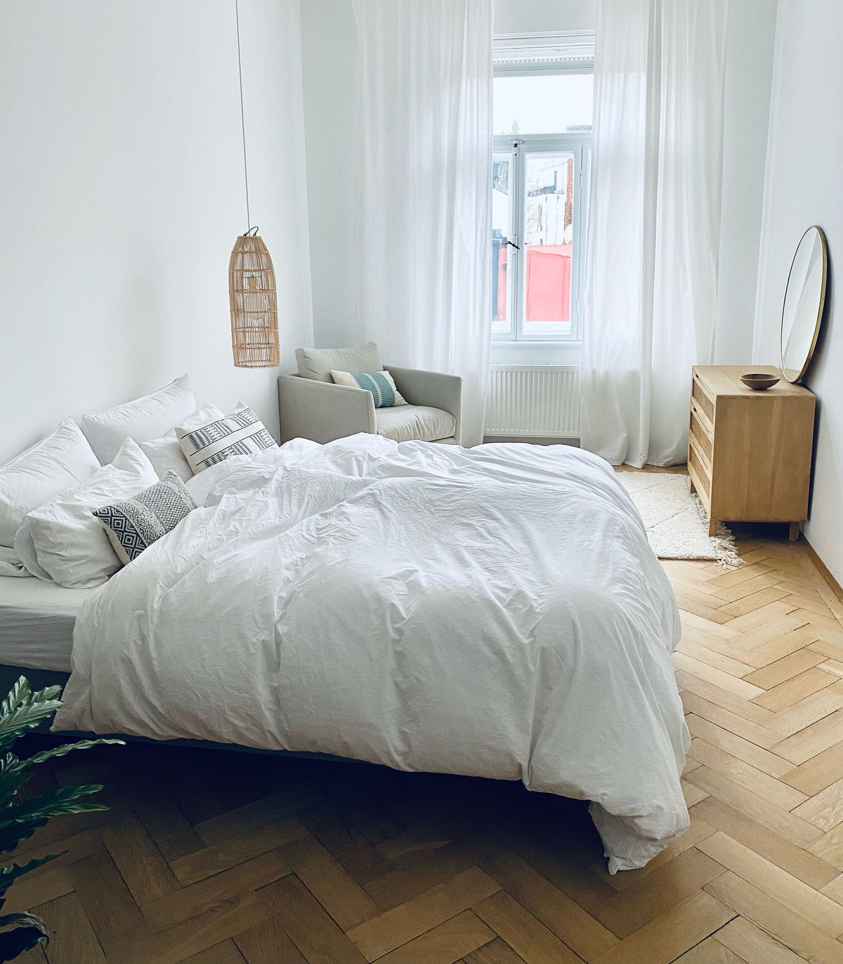 Gemütliche Schlafzimmereinrichtung im Scandiboho Style. Beni Qurain Teppich mit Rattankommode und Rattanlampenschirm. Weiße Bettwäsche rundet die Schlafzimmereinrichtung ab. 